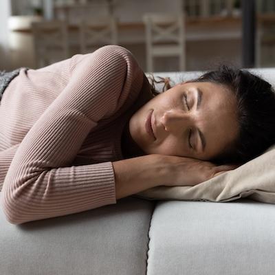 Erschöpfte Frau liegt schlafend auf einem Sofa, symbolisch für starke Müdigkeit und medizinische Labordiagnostik zur Analyse möglicher Ursachen wie Hormonstörungen, Eisenmangel oder Stoffwechselprobleme.